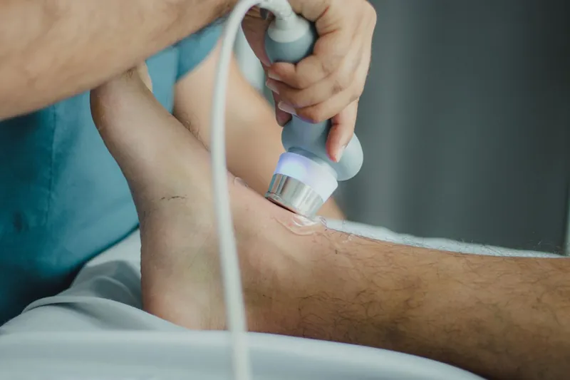 Fisioterapista che applica il manipolo di una terapia strumentale sulla caviglia di un paziente